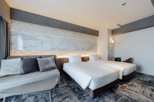 A modern hotel room with a large bed, a sofa, a small table, and a marble accent wall.