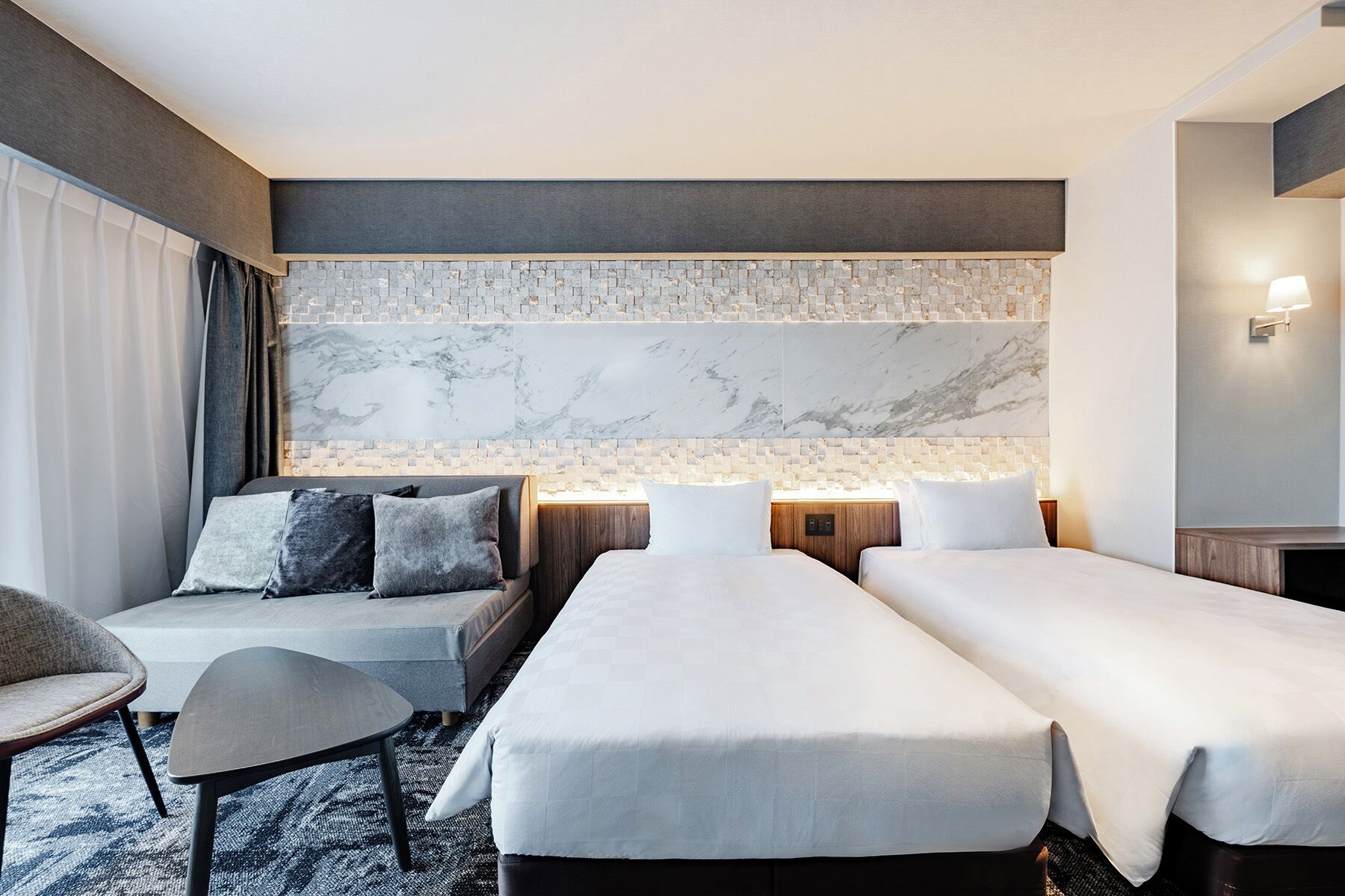 A hotel room with a large bed, a smaller sofa, and a desk.