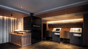 Et receptionsområde med en træreception, en digital kiosk og et skilt med teksten "The OneFive Osaka Shinkinai".