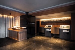 A reception area with a wooden reception desk, a digital kiosk, and a sign reading "The OneFive Osaka Shinkinai".