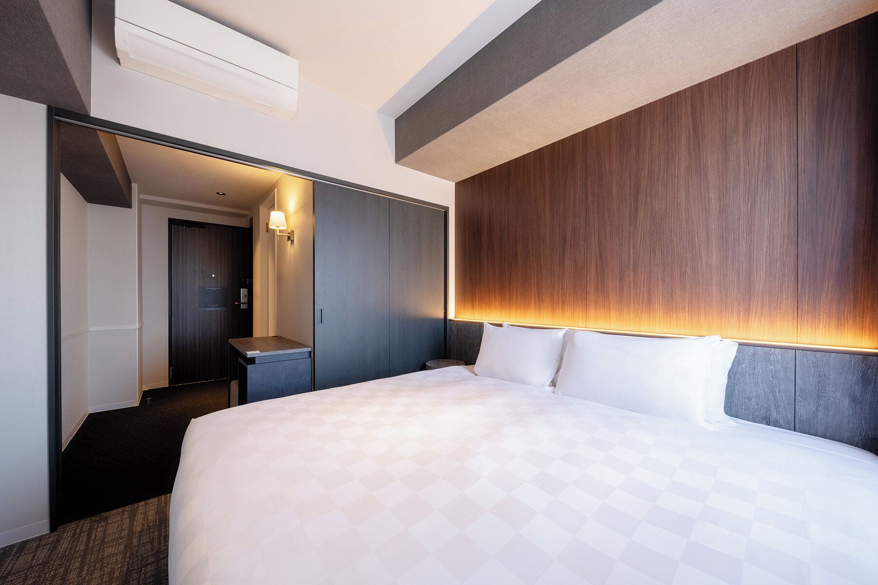 Una habitación de hotel moderna con una cama grande, un cabecero de madera, un escritorio y un espejo.