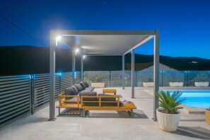 An outdoor seating area with a pool, covered by a modern structure, and surrounded by a metal fence. - Family Holiday Home in Tugare With Pool (Omis)