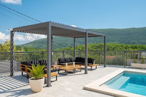 Ett takförsett utomhusområde med sittplatser, en pool och utsikt över bergen.