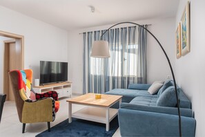 Ett modernt vardagsrum med en platt-TV, en färgglad fåtölj, en blå soffa och en golvlampa.