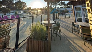 An outdoor patio area with tables and chairs, a wooden pergola, and a view of a playground in the background. - At "Greg and Ilhem (Lège-Cap-Ferret)