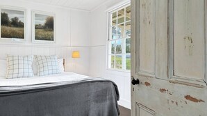 Um quarto com cama, duas janelas, abajur e porta.