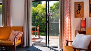 Een kamer met een bank, een stoel, een tafel en uitzicht op een tuin door een schuifdeur.