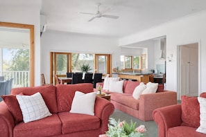 Ein geräumiger Wohnbereich mit zwei roten Sofas, einem Esstisch und einer Küche im Hintergrund.