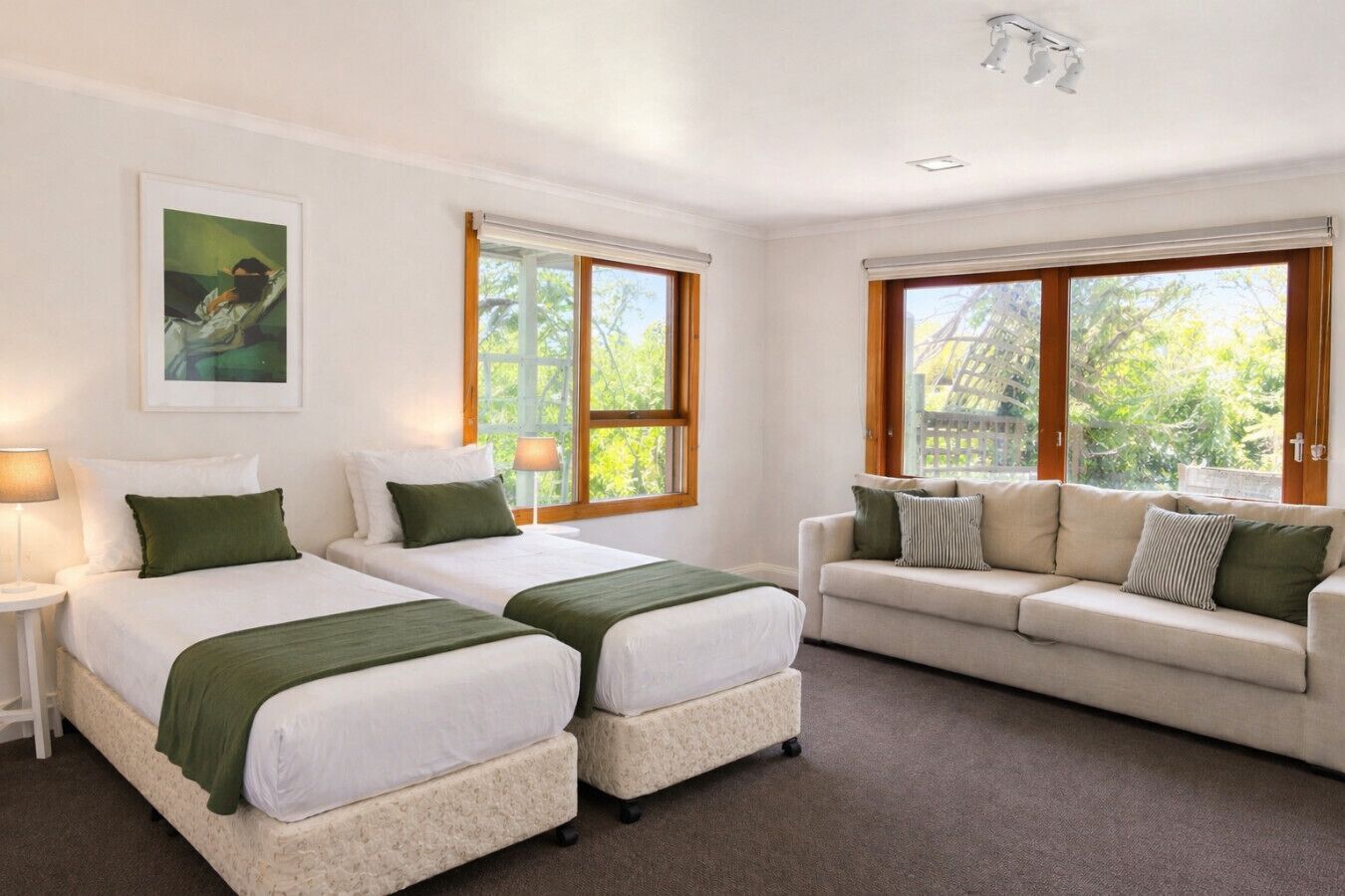 Habitación de hotel con dos camas, un sofá y ventanas amplias con persianas.