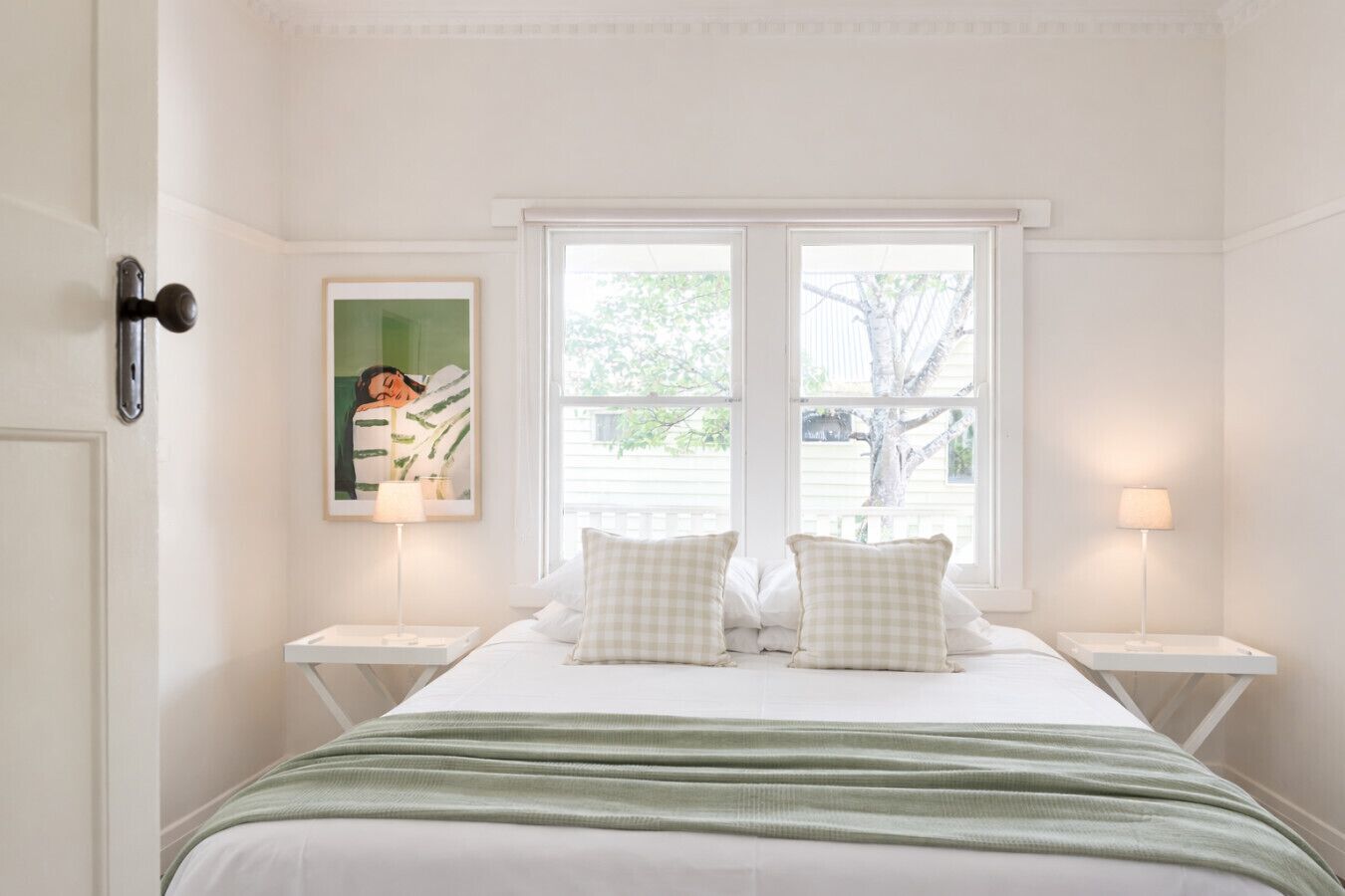A bedroom with a bed, two bedside tables, a window, and a framed picture on the wall.