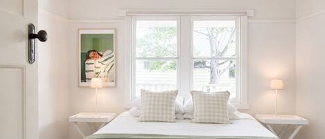 A bedroom with a bed, two bedside tables, a window, and a framed picture on the wall.