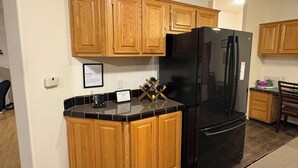 A compact kitchen with wooden cabinets, a black refrigerator, and a countertop with wine bottles. - Cozy, Spacious 3BR Retreat in North Albany Family-Friendly, Near OSU & Wineries (Albany)