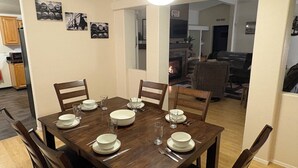 A dining area with a wooden table set for four, surrounded by chairs. There are framed pictures on the wall, a sign indicating a movie room, and a fireplace in the background. - Cozy, Spacious 3BR Retreat in North Albany Family-Friendly, Near OSU & Wineries (Albany)