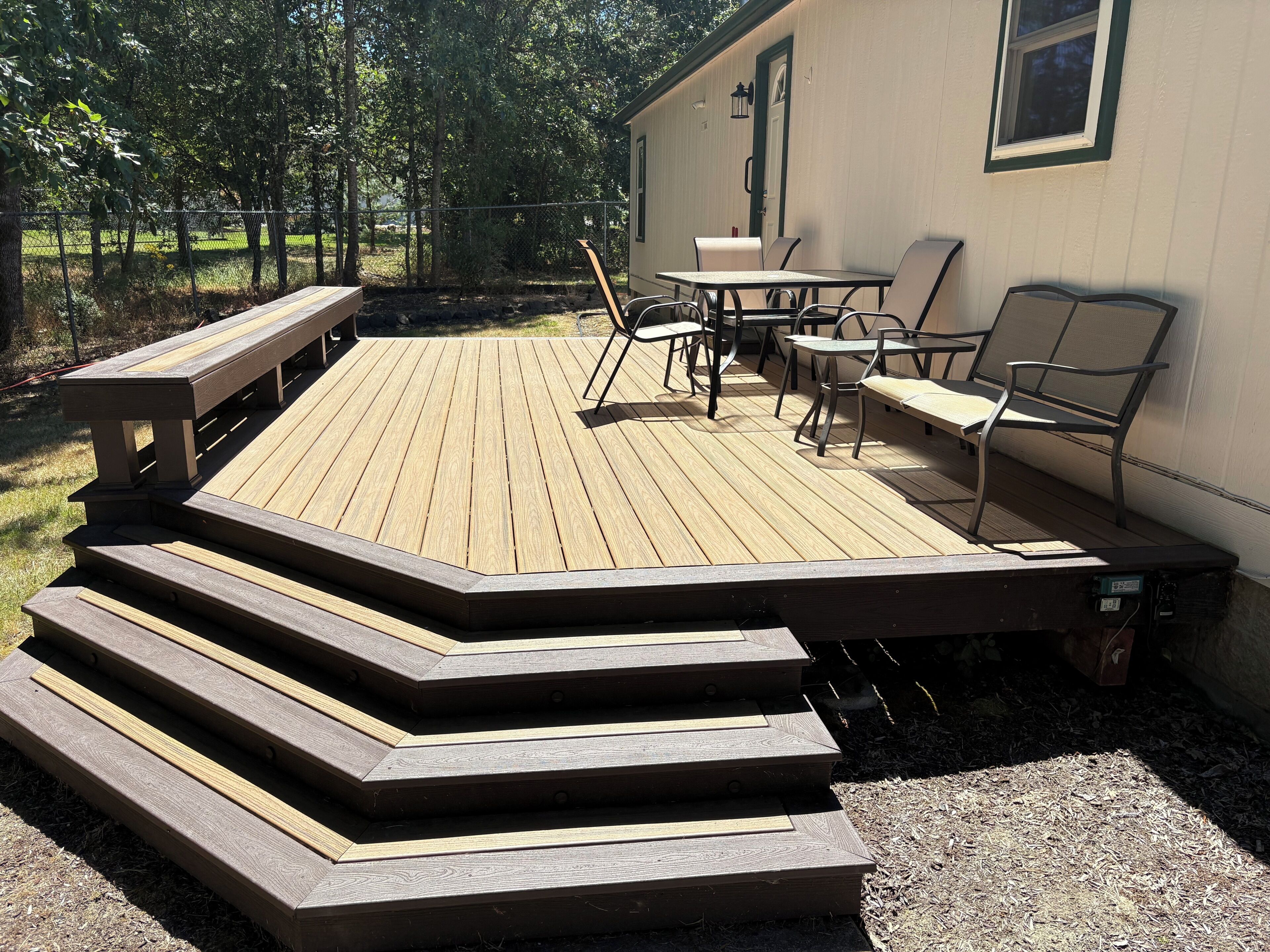 A wooden deck with a table and chairs, a bench, and a small outdoor kitchen area.