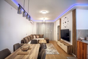 Un salon moderne avec une table à manger en bois, un canapé et un téléviseur fixé au mur.