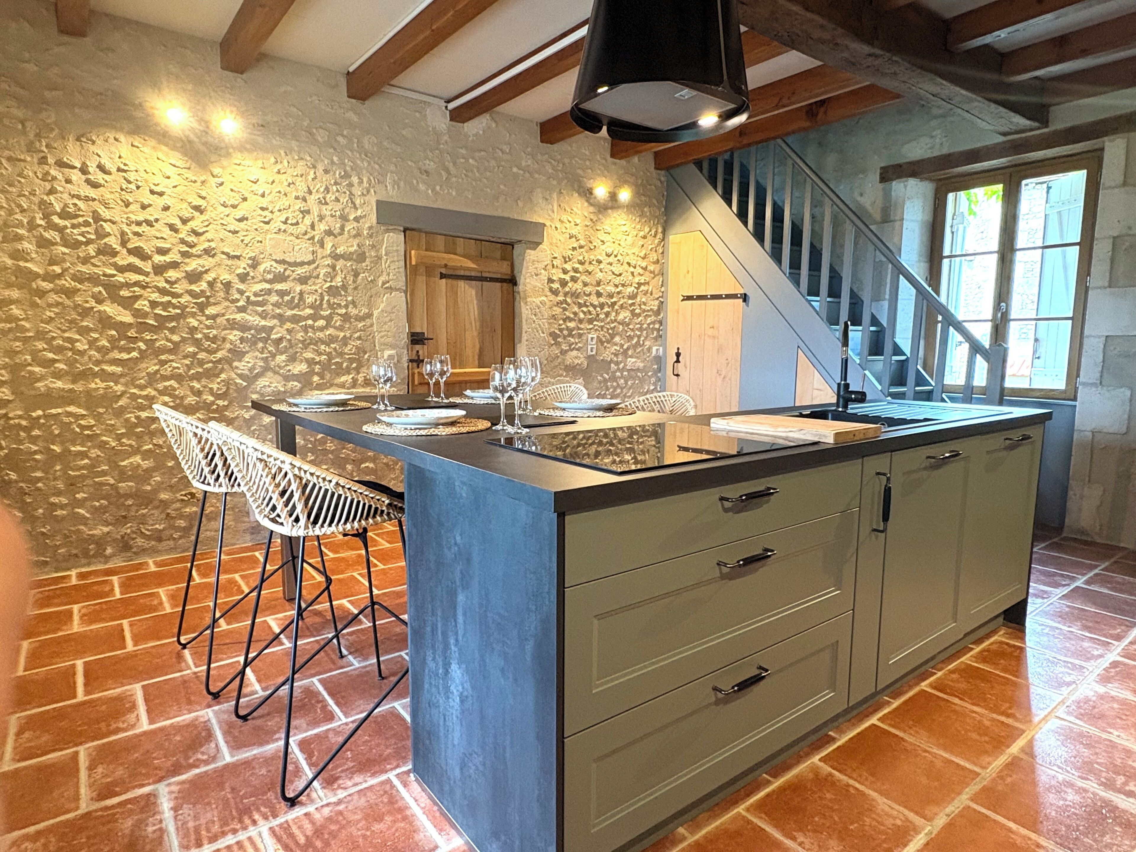 Una cocina con una isla central, paredes de piedra y una escalera que sube a un nivel superior.