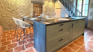 Una cocina con una isla central, paredes de piedra y una escalera que sube a un nivel superior.