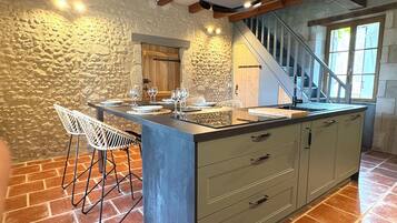 Una cocina con una isla central, paredes de piedra y una escalera que sube a un nivel superior.
