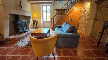 Un salon chaleureux avec une cheminée, un canapé, un fauteuil jaune et un escalier.