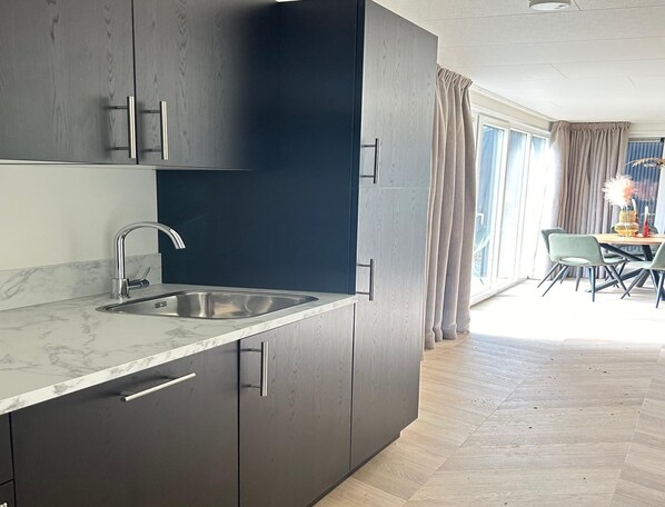 A modern kitchen with dark cabinets, a marble countertop, and a sink. - Pleasant Home by Palette Resort De-steppe (Ulicoten)