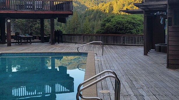 Une terrasse en bois avec une piscine, offrant une vue sur une chaîne de montagnes boisées.