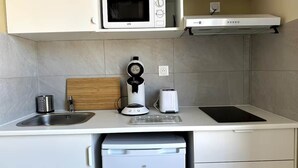 Een kleine keuken met een magnetron, broodrooster, koffiezetapparaat en een spoelbak.