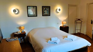 Ein ordentlich bezogenes Bett mit weißen Leinen und Handtüchern, zwei Nachttischlampen und gerahmte Bilder an der Wand.