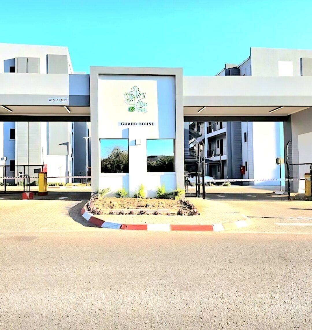 A modern building with a 'GUARD HOUSE' sign, a 'VISITORS' sign, and a landscaped area with plants.