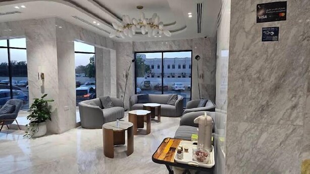 A spacious, modern lounge area with marble flooring, comfortable seating, and a view of the parking lot. - Alyas Hotel (Muscat)