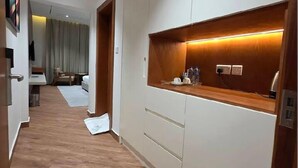 A hallway with a wooden floor, a built-in bench, and a wall-mounted shelf with a light. - Alyas Hotel (Muscat)