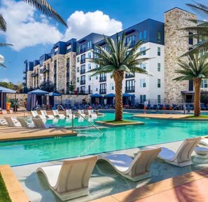 Un espace piscine doté de chaises longues, de palmiers et d’un bâtiment avec de nombreux balcons.