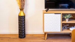 Un salon avec un plancher en bois, un téléviseur posé sur un meuble en bois, une armoire blanche et un vase contenant des plantes séchées.