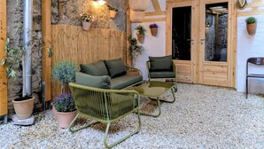 Un intérieur rustique avec des éléments en bois, un mur en pierre, un canapé vert, un fauteuil en osier et des plantes en pot.