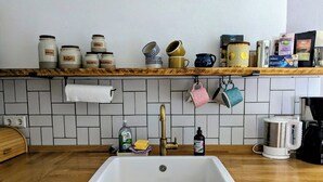 Une cuisine avec un plan de travail en bois, un évier blanc et divers ustensiles de cuisine rangés sur une étagère.