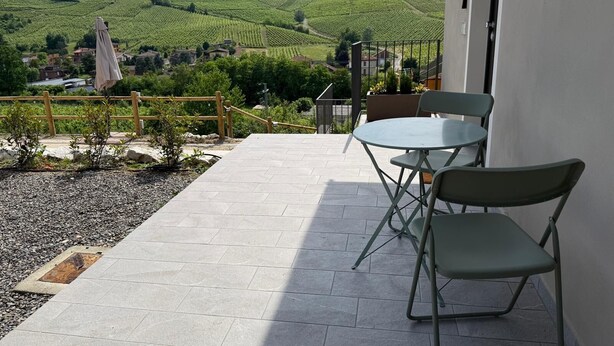A terrace with a table and chairs, a view of vineyards, and a building in the background. - Welcoming accommodation with panoramic views for your stay in Oltrepò Pavese (Torricella Verzate)