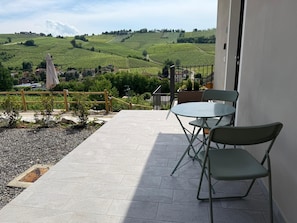 A terrace with a table and chairs, a view of vineyards, and a building in the background. - Welcoming accommodation with panoramic views for your stay in Oltrepò Pavese (Torricella Verzate)