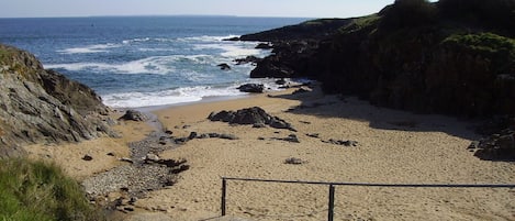 A coastal beach with a rocky shoreline, a sandy path leading to the beach, and a clear view of the ocean.