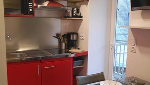 Uma cozinha compacta com micro-ondas, fogão e máquina de café. Há uma mesa de jantar posta com pratos, talheres e copos.