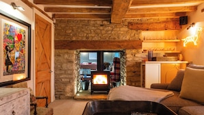 A cozy living room with a stone wall, wooden beams, a fireplace, a sofa, a coffee table, and a framed artwork. - Stunning 6 BB Cottage & Annexe  (Little Milton)