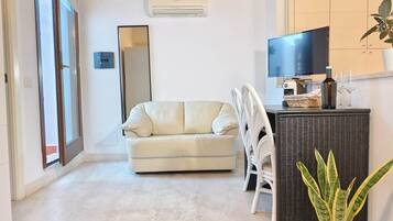 A living room with a sofa, a chair, a television, and a potted plant.
