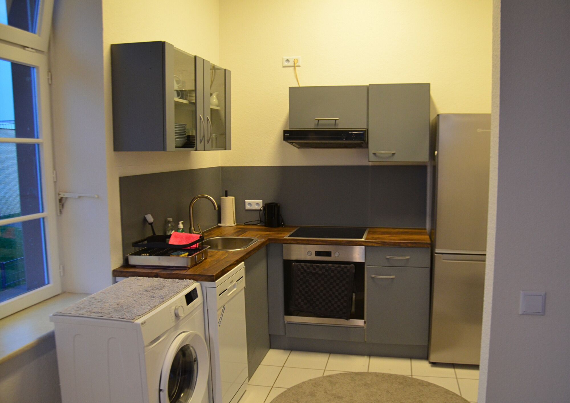Una cocina compacta equipada con lavadora, horno empotrado, microondas y refrigerador.