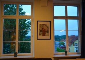 A room with two large windows, a framed picture on the wall, and a small plant on the windowsill.