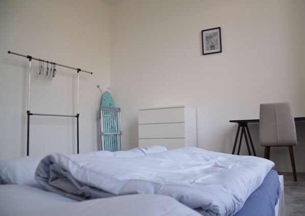 A bedroom with a bed, a desk, a chair, a radiator, and a framed picture on the wall.