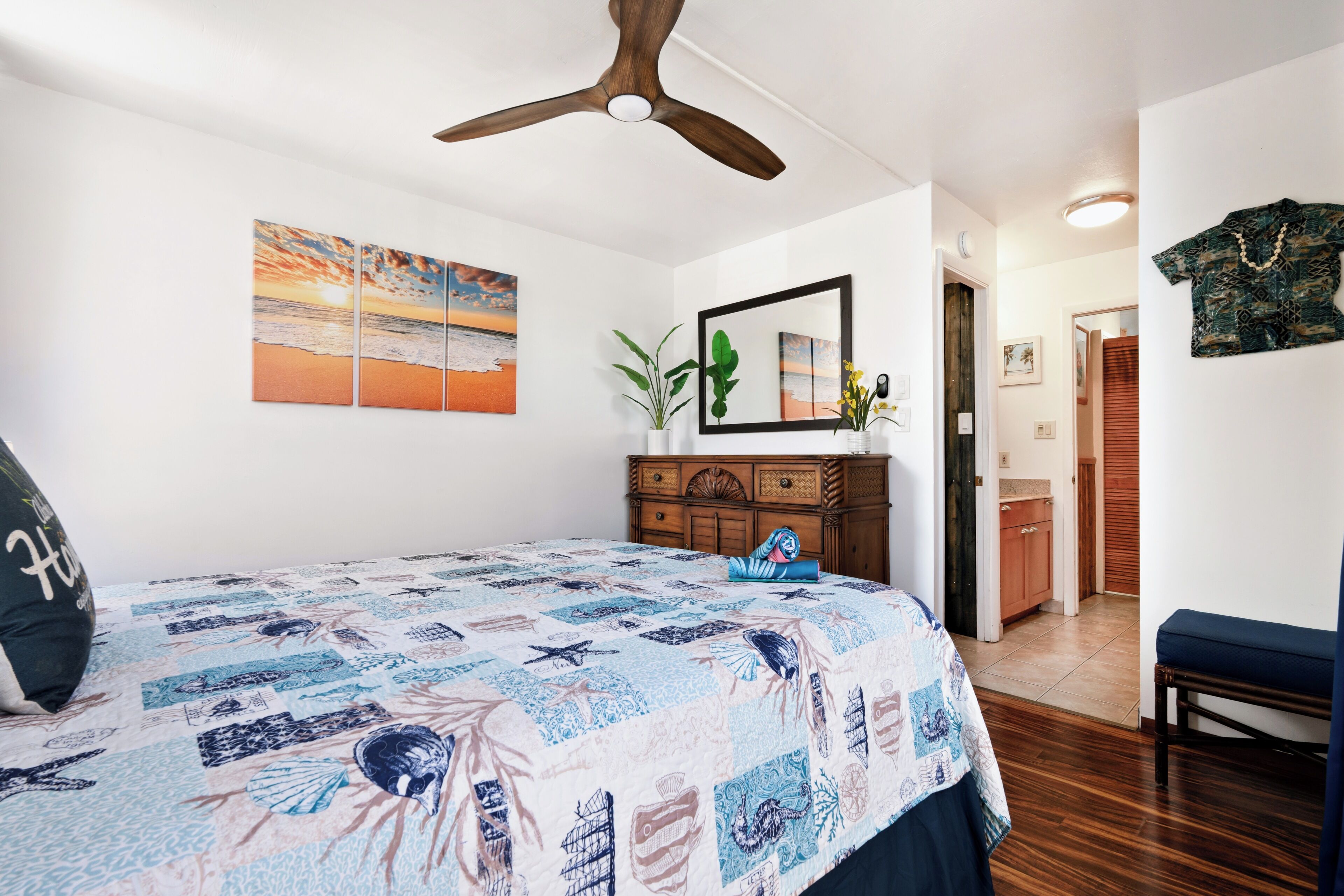 A bedroom with a bed, a ceiling fan, a dresser, a mirror, and a door leading to a bathroom.