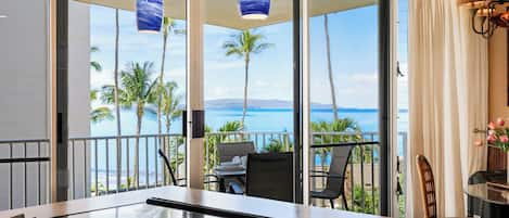 A dining area with a view of the ocean and palm trees.
