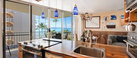 A modern kitchen with a built-in dishwasher, a large island with a sink, and a view of the ocean through large windows.