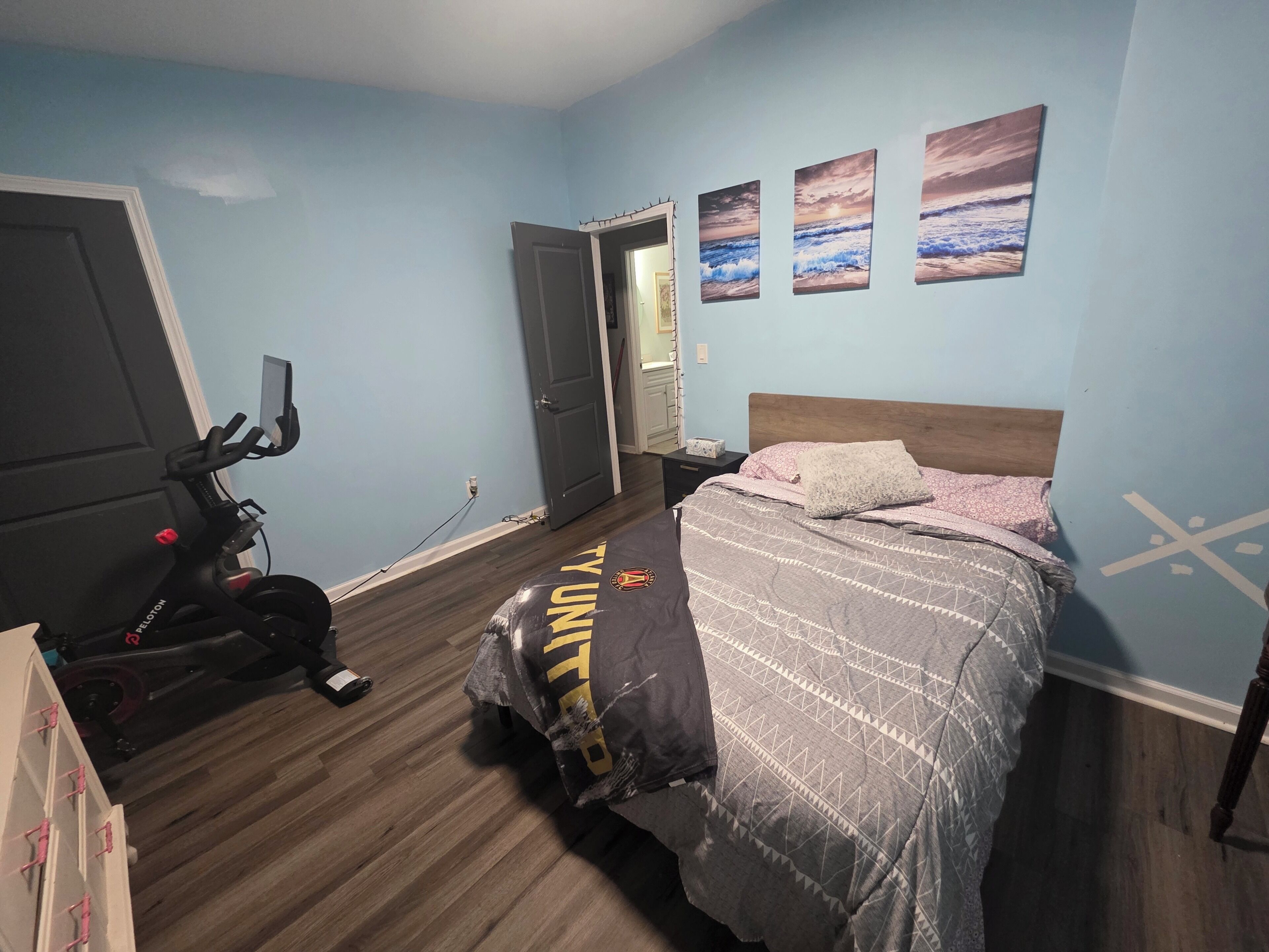 Un dormitorio con cama, televisor montado en la pared y puerta que da a otra habitación.