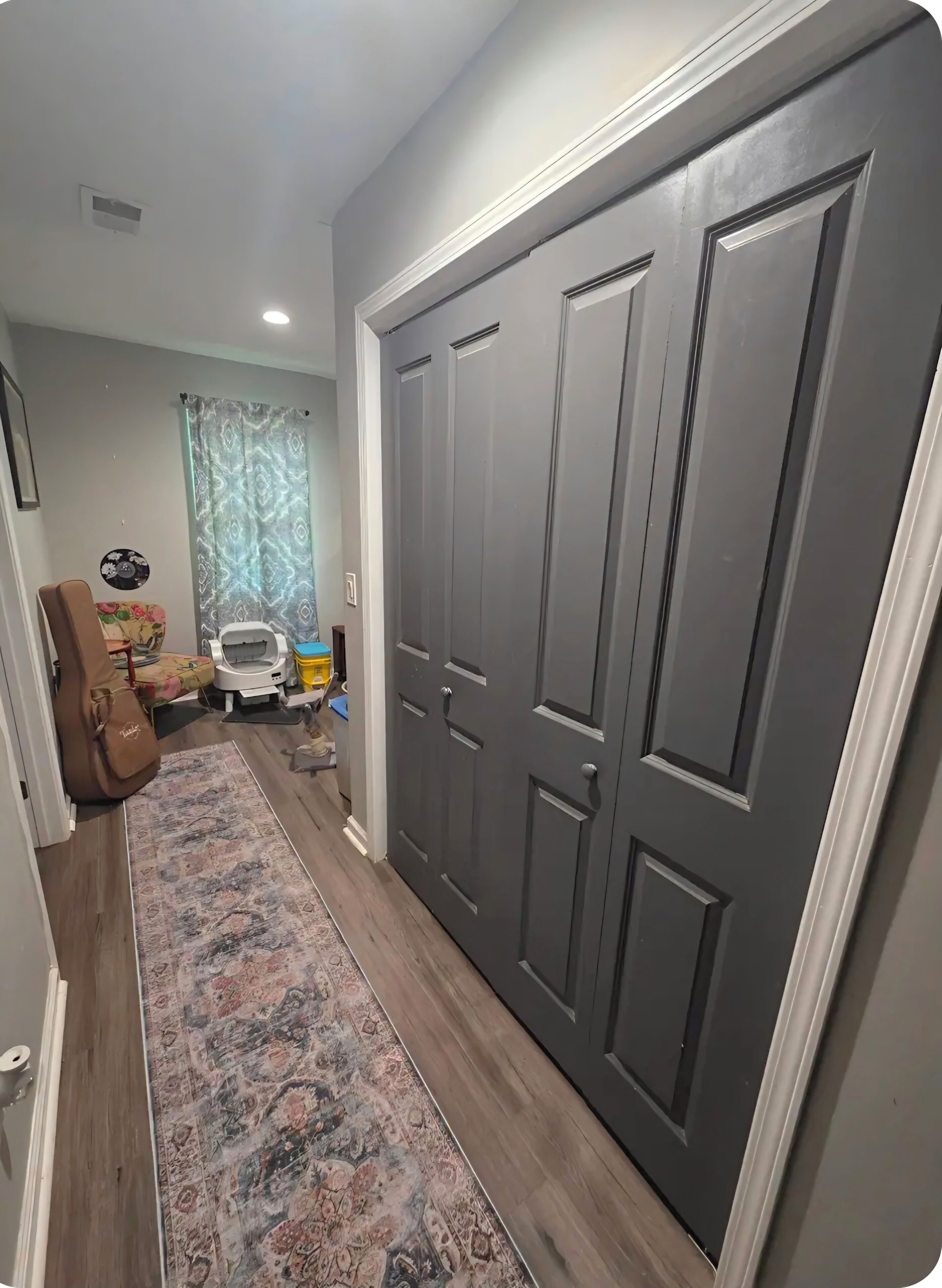 A hallway with a patterned rug, a dark wooden door, and a small white chair.