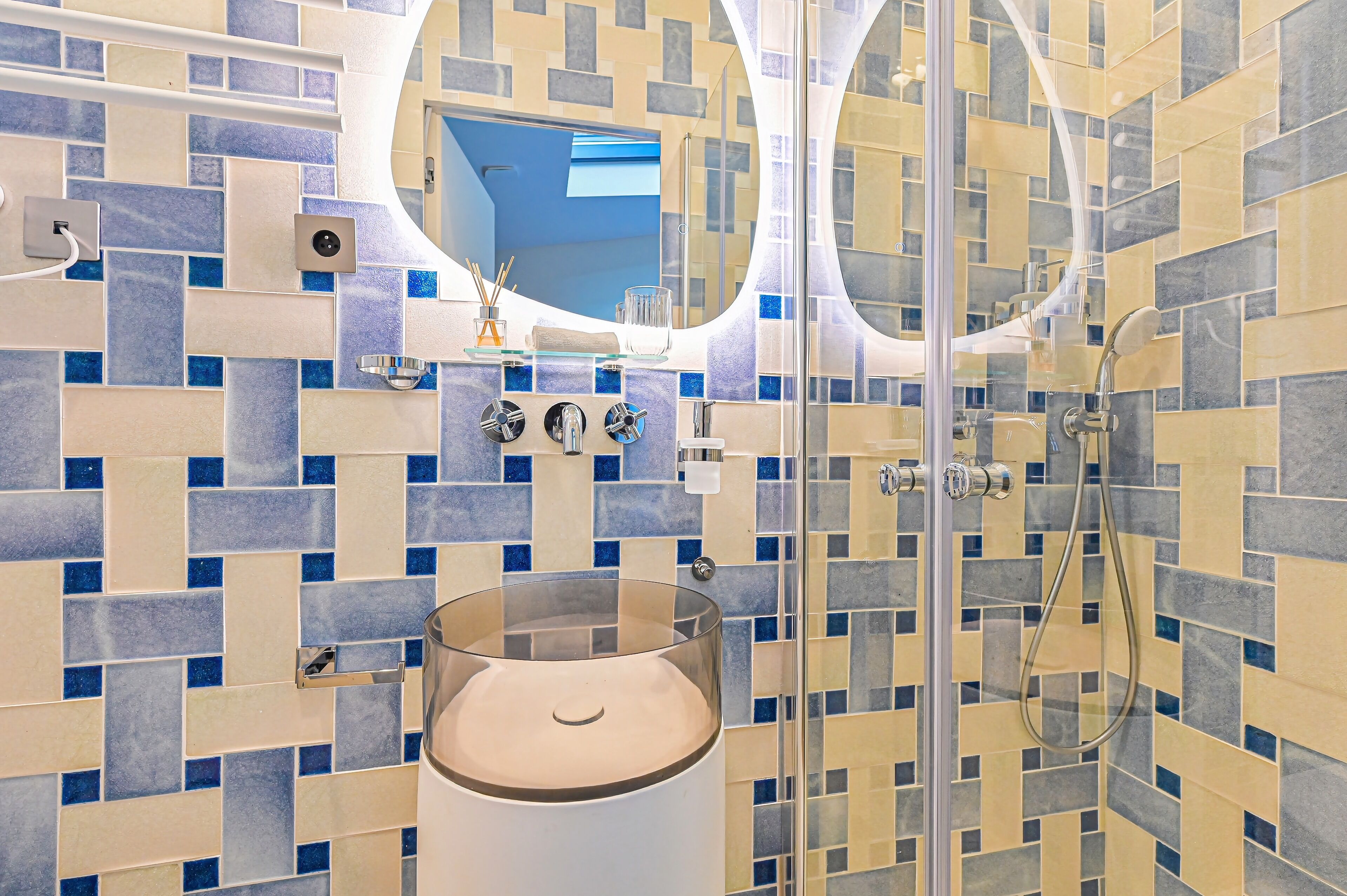 Un baño con un lavabo de vidrio, un espejo y una zona de ducha.