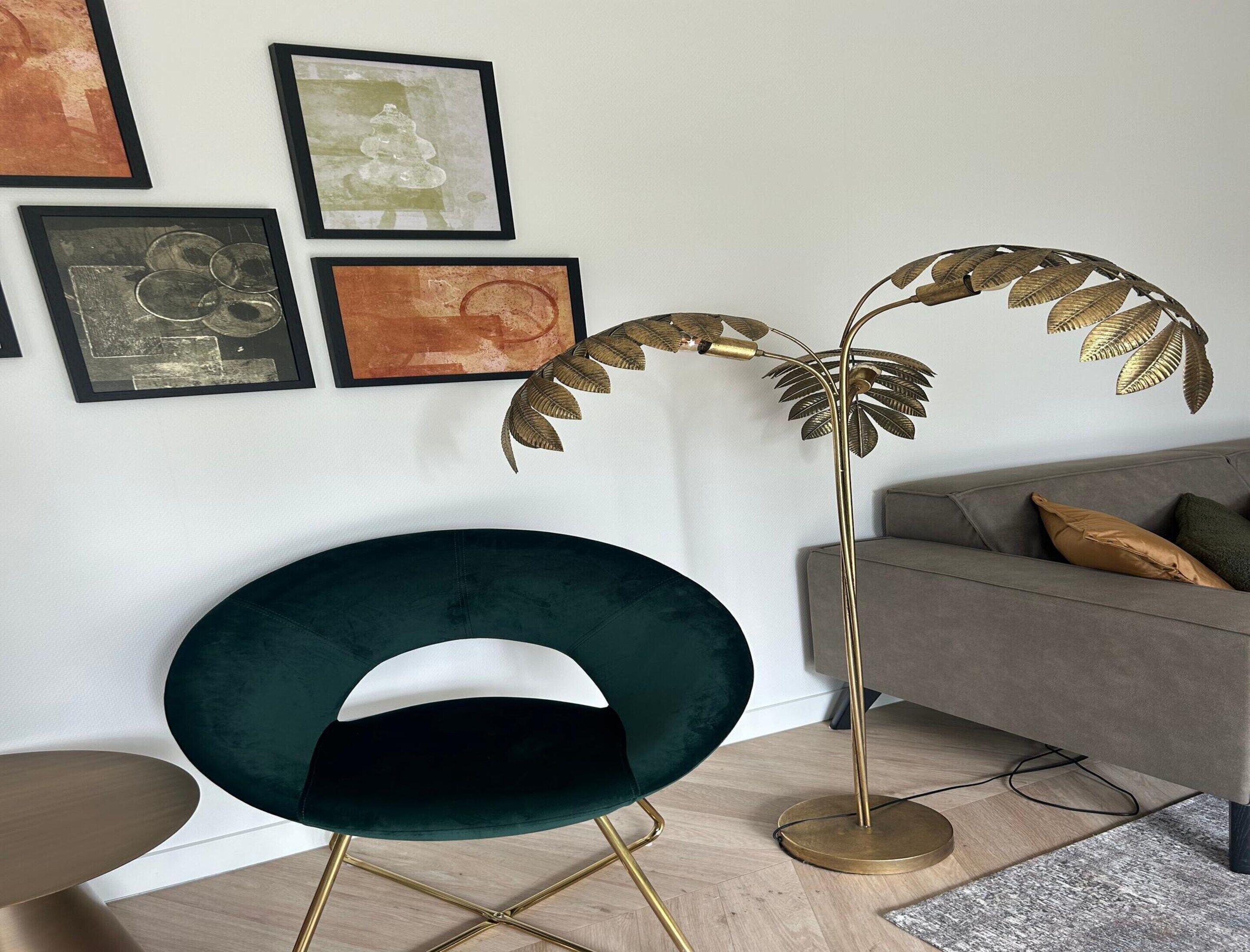 Una sala de estar moderna con un sillón verde oscuro, una lámpara de pie dorada y un sofá gris con cojines.